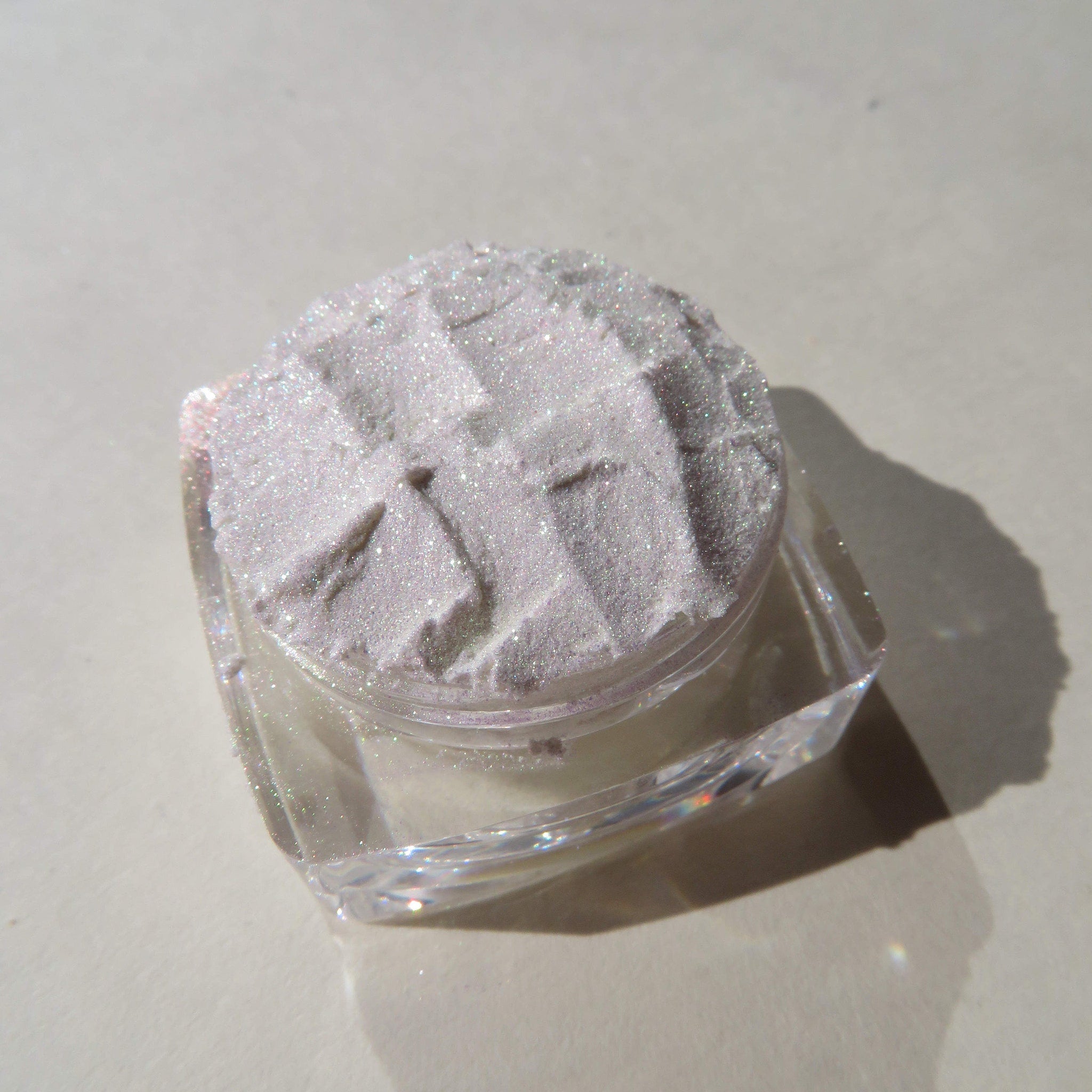 Hand applying white shimmer eyeshadow with green gold sheen using a fluffy brush on eyelid