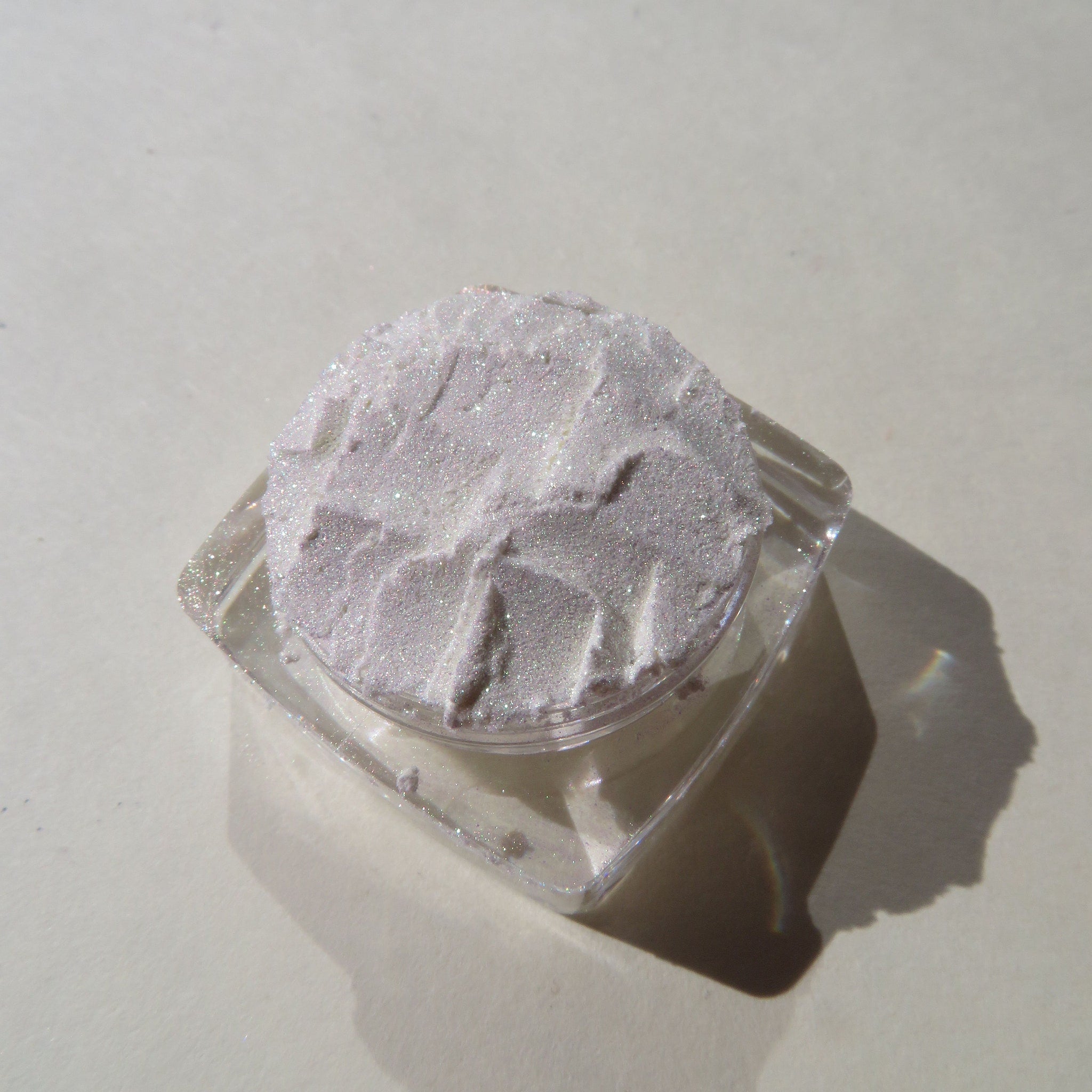 Close-up of loose white shimmer eyeshadow with green gold sheen, showcasing fine pigment texture