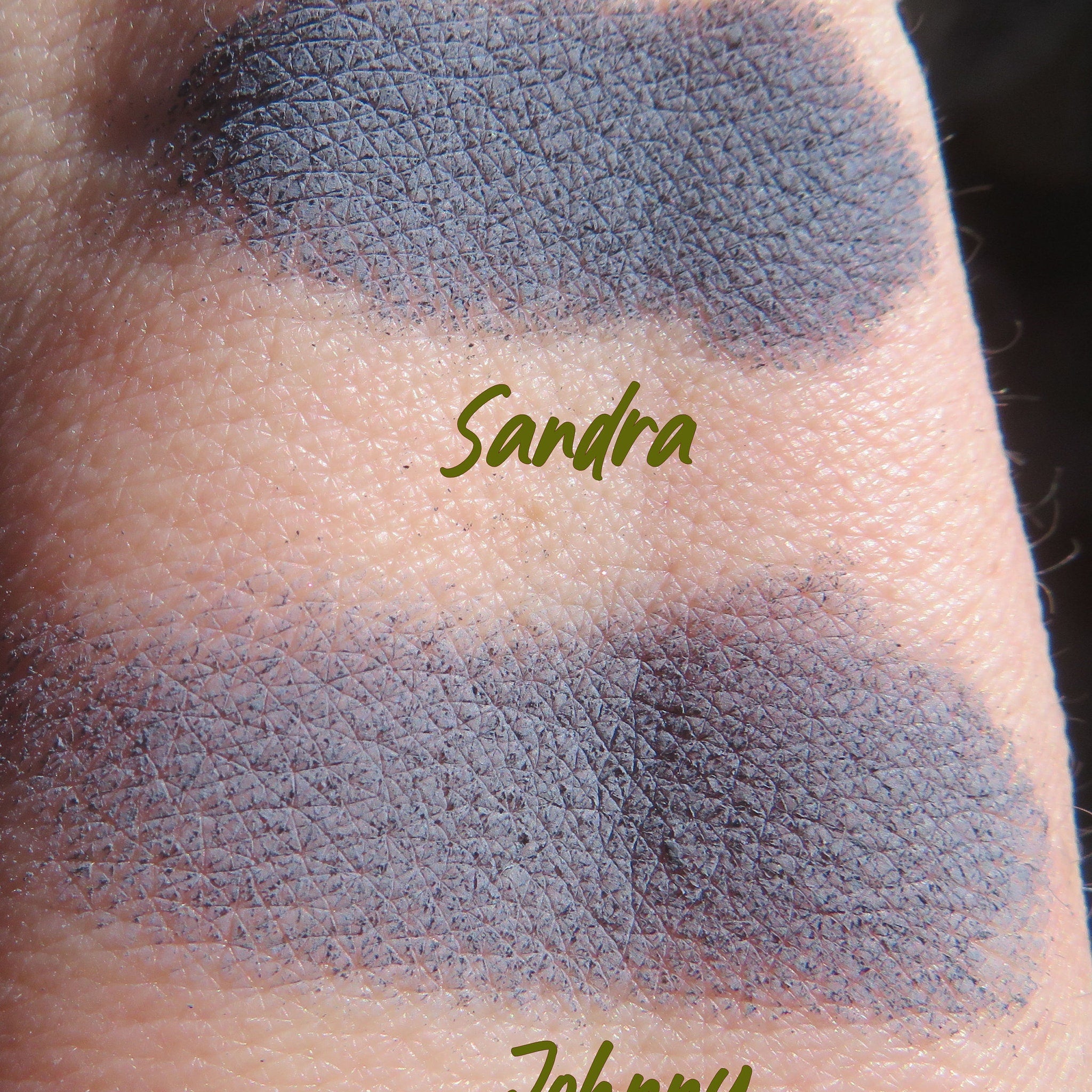 Eye shadow swatch with blue-gray color and textured pattern on skin, with "Sandra" text visible