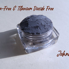 Dark gray powder in a clear glass jar with a textured surface, on a white background