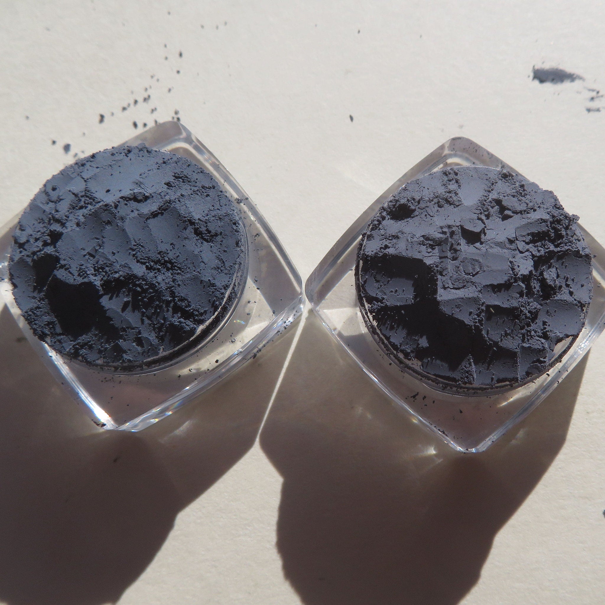 Powder pigment in dark gray color, contained in clear square containers, on a light surface