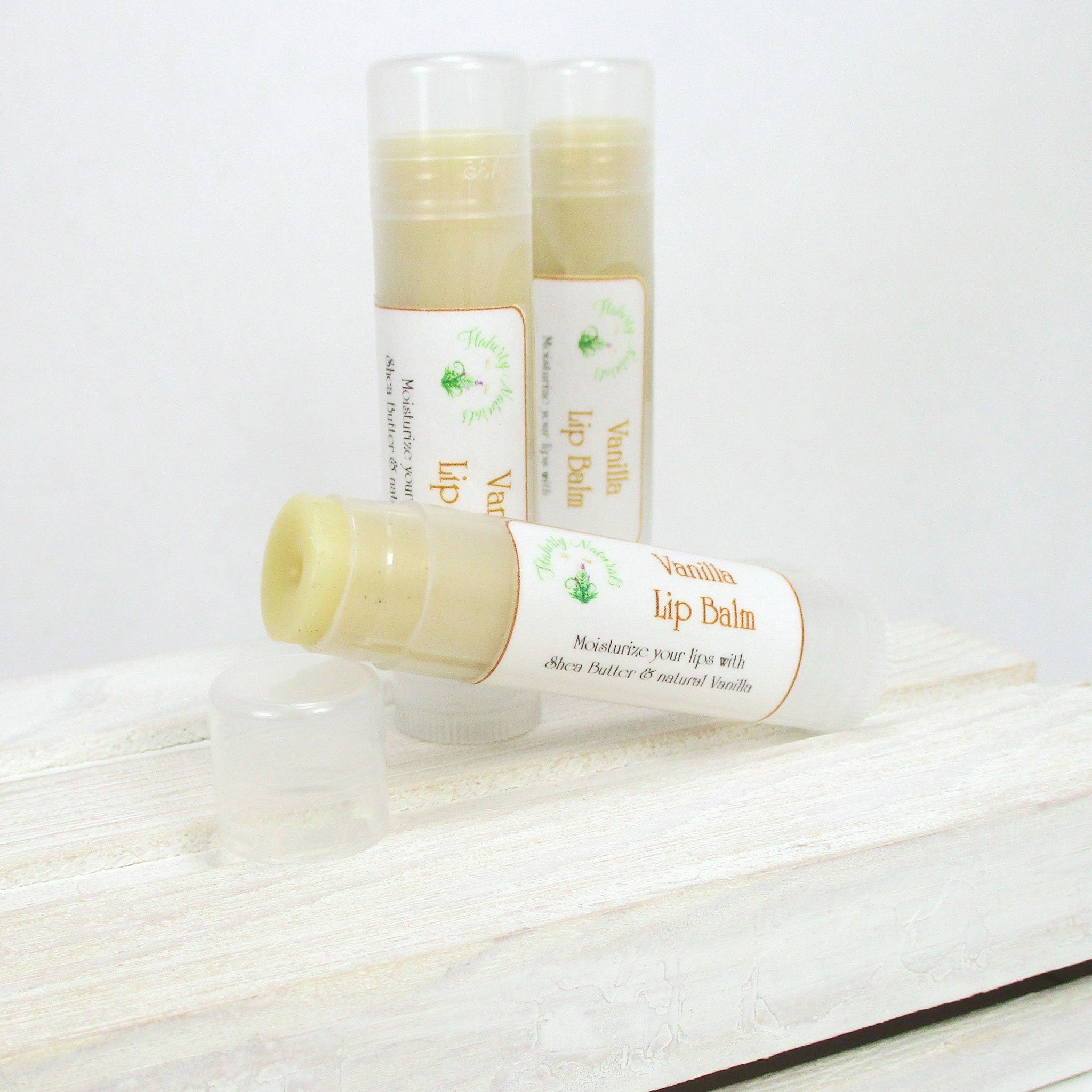 Lip balm tubes with white and tan labels, partially open on white wood surface