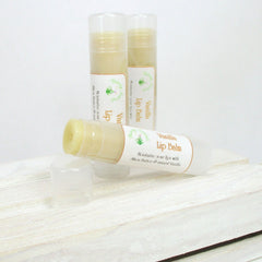 Lip balm tubes with white and tan labels, partially open on white wood surface