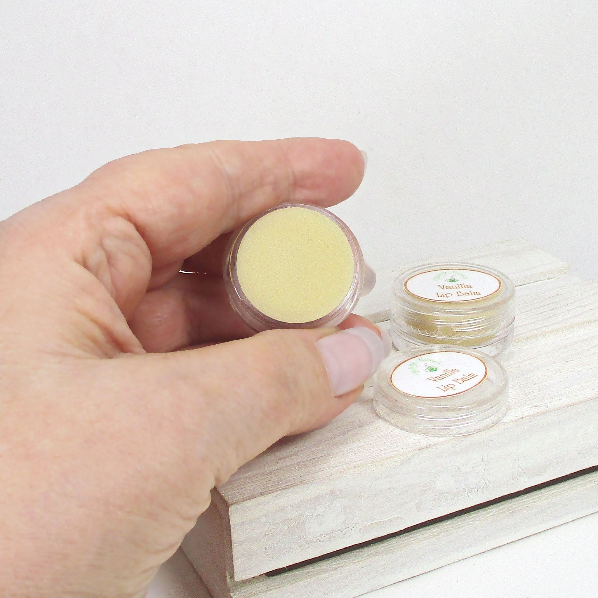 Lip balm in clear plastic containers with yellow balm and white labels, held by hand