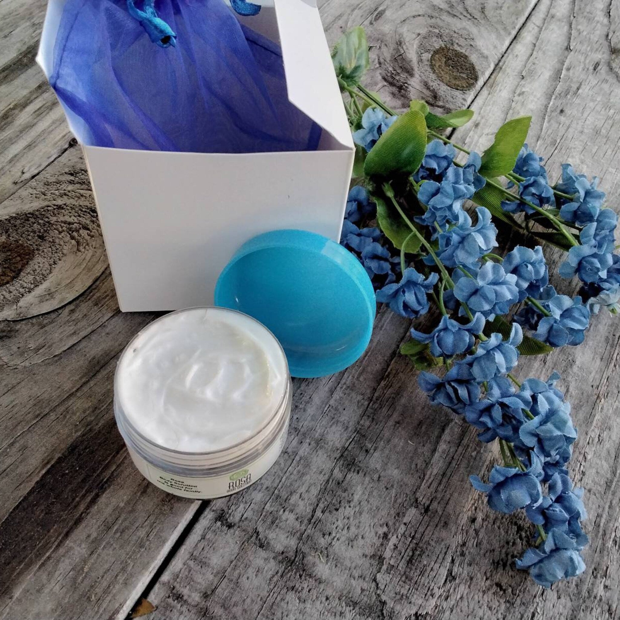 Cream jar with white cream, blue lid, and blue flowers on wooden surface