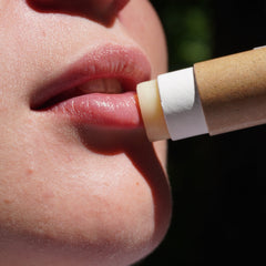 Lip balm being applied, beige and white tube, clear balm on lips