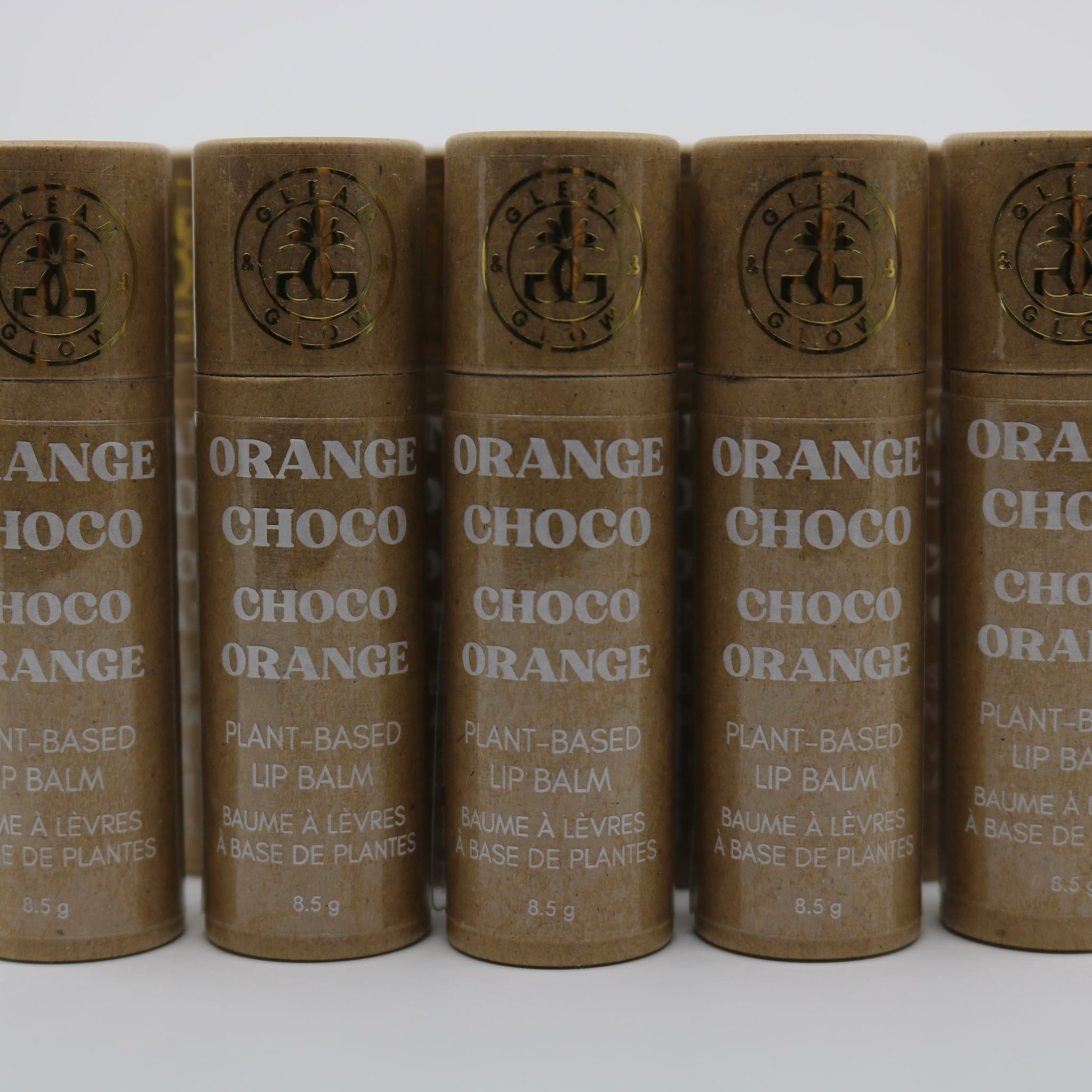 Lip balm tubes, brown paper material, white text, "GLEAM & GLOW" brand logo visible