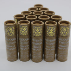 Lip balm tubes in brown cardboard with gold logo and text, stacked in pyramid formation