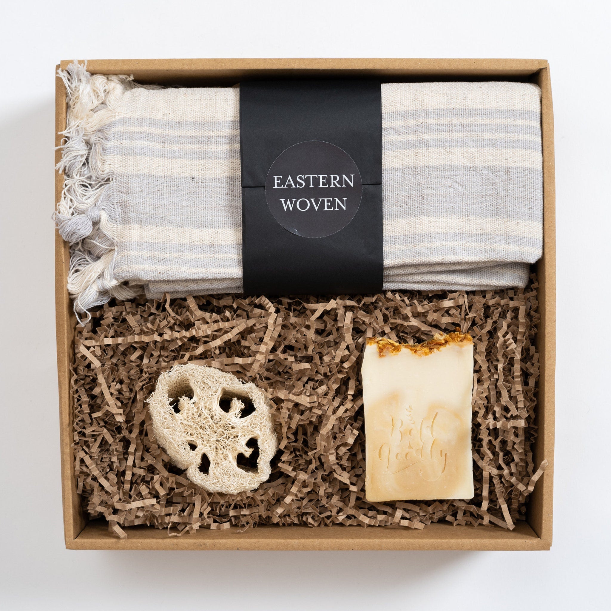 Gift box with gray striped towel, natural soap, and loofah, "Eastern Woven" label visible