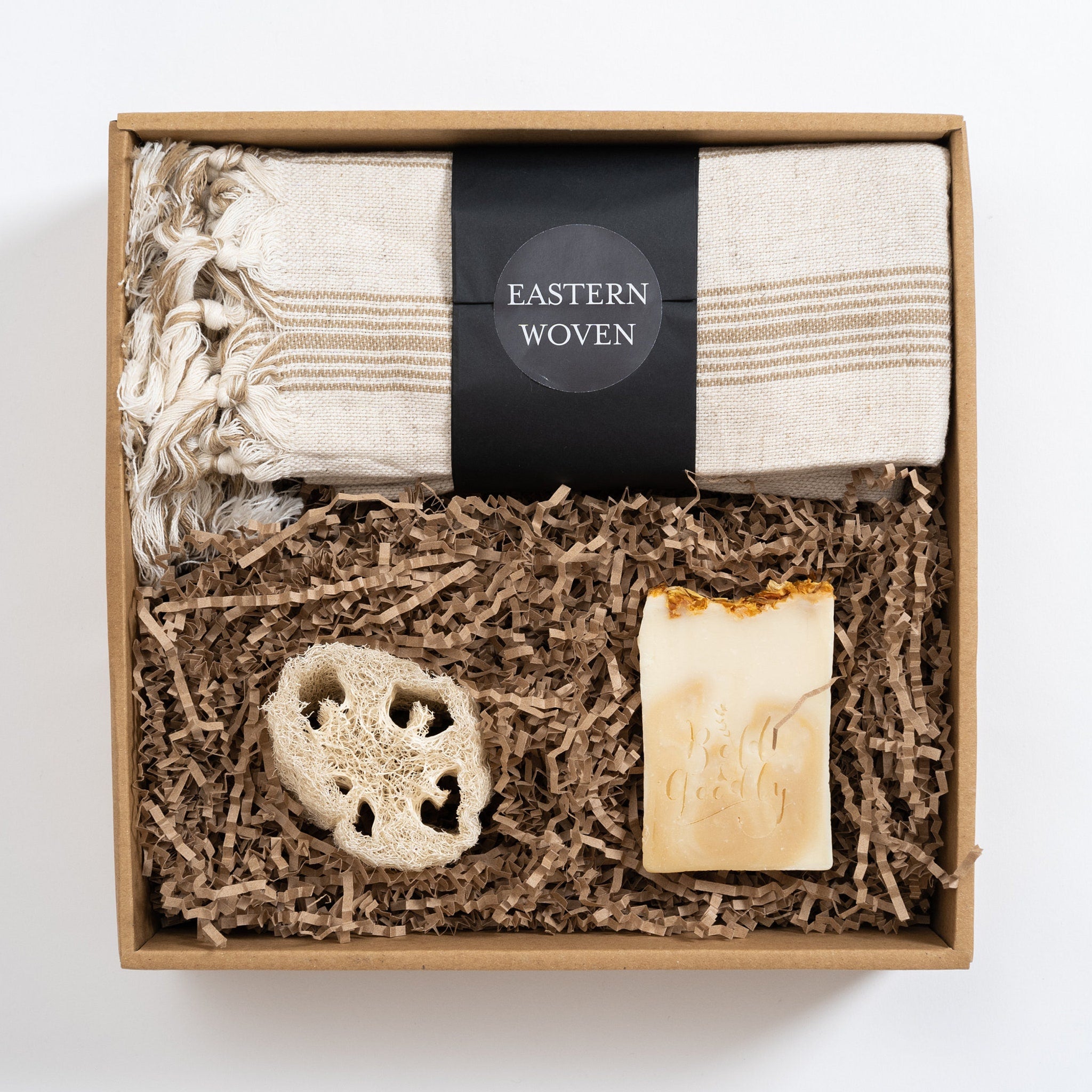 Gift set with beige striped towel, soap, loofah, and "EASTERN WOVEN" label in a brown box.
