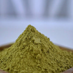 Green powder pile, fine texture, close-up view, in a wooden bowl