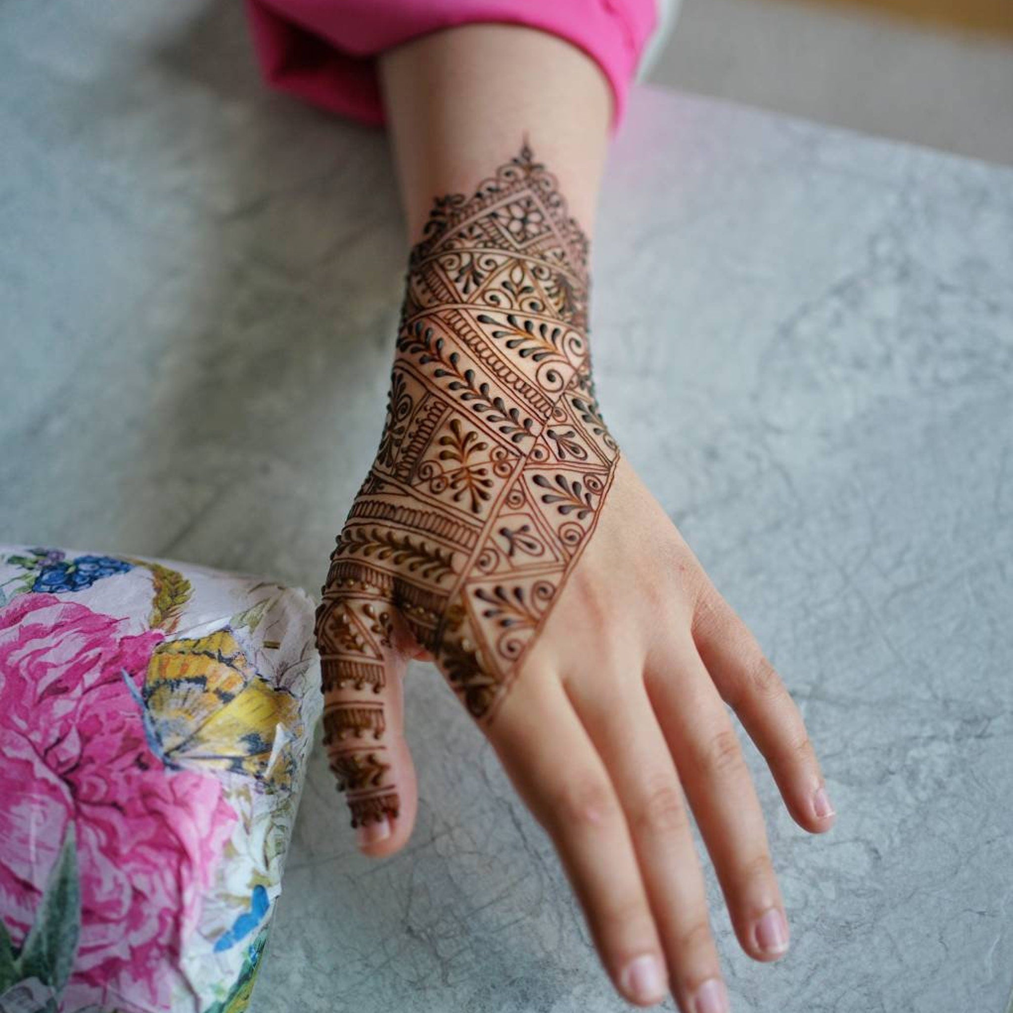 Henna tattoo brown pattern on hand with floral design, pink sleeve visible