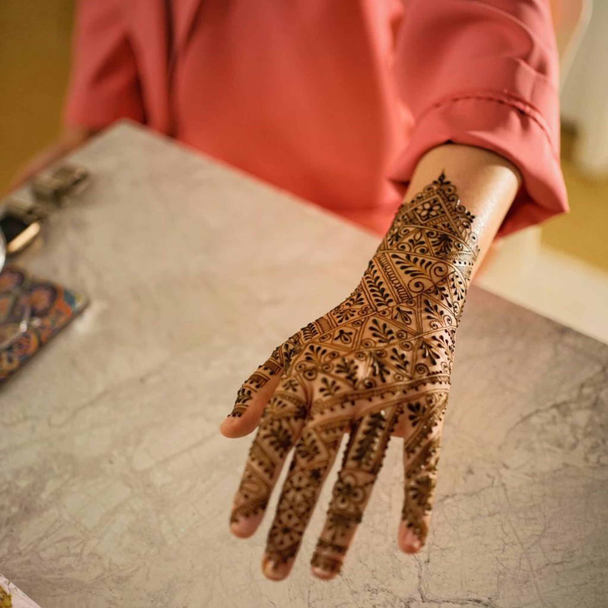 Henna hand art with brown intricate pattern on skin, with pink sleeve in background