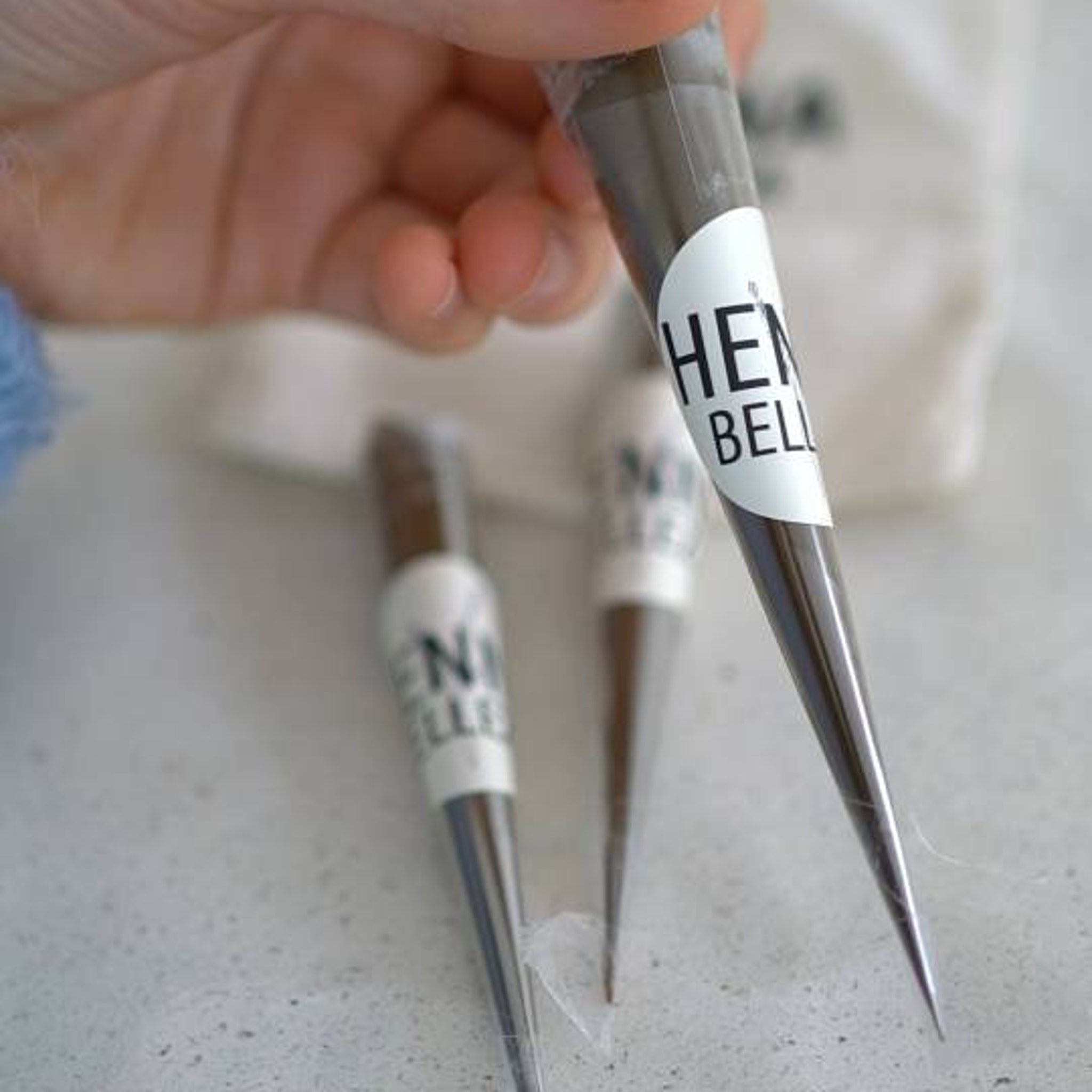 Henna cones with brown paste, white label, held in hand, "HENNA BELLE" brand visible