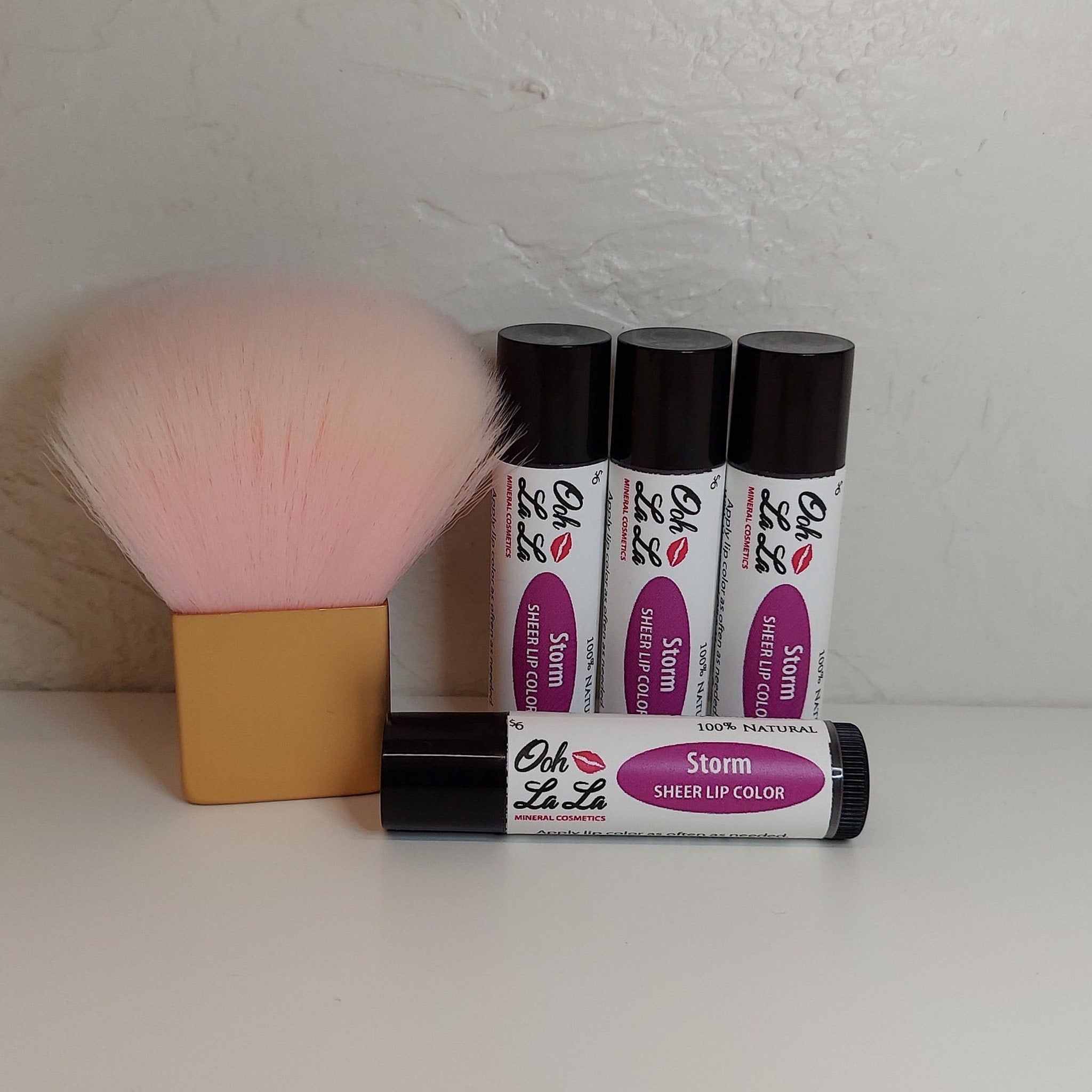 Lip color tubes with black caps, white labels, and "Ooh La La" brand text, and a pink makeup brush