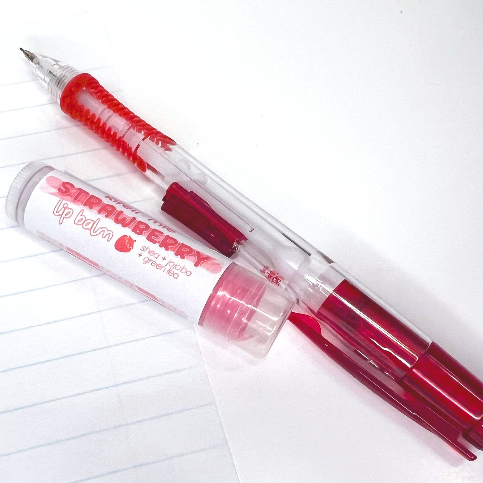 Lip balm tube with red accents and clear plastic, next to a red and clear mechanical pencil on lined paper
