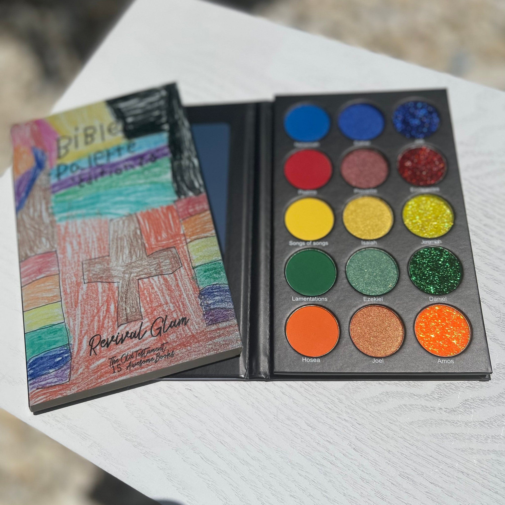 Eyeshadow palette with colorful eyeshadows, black case, and Revival Glam book cover