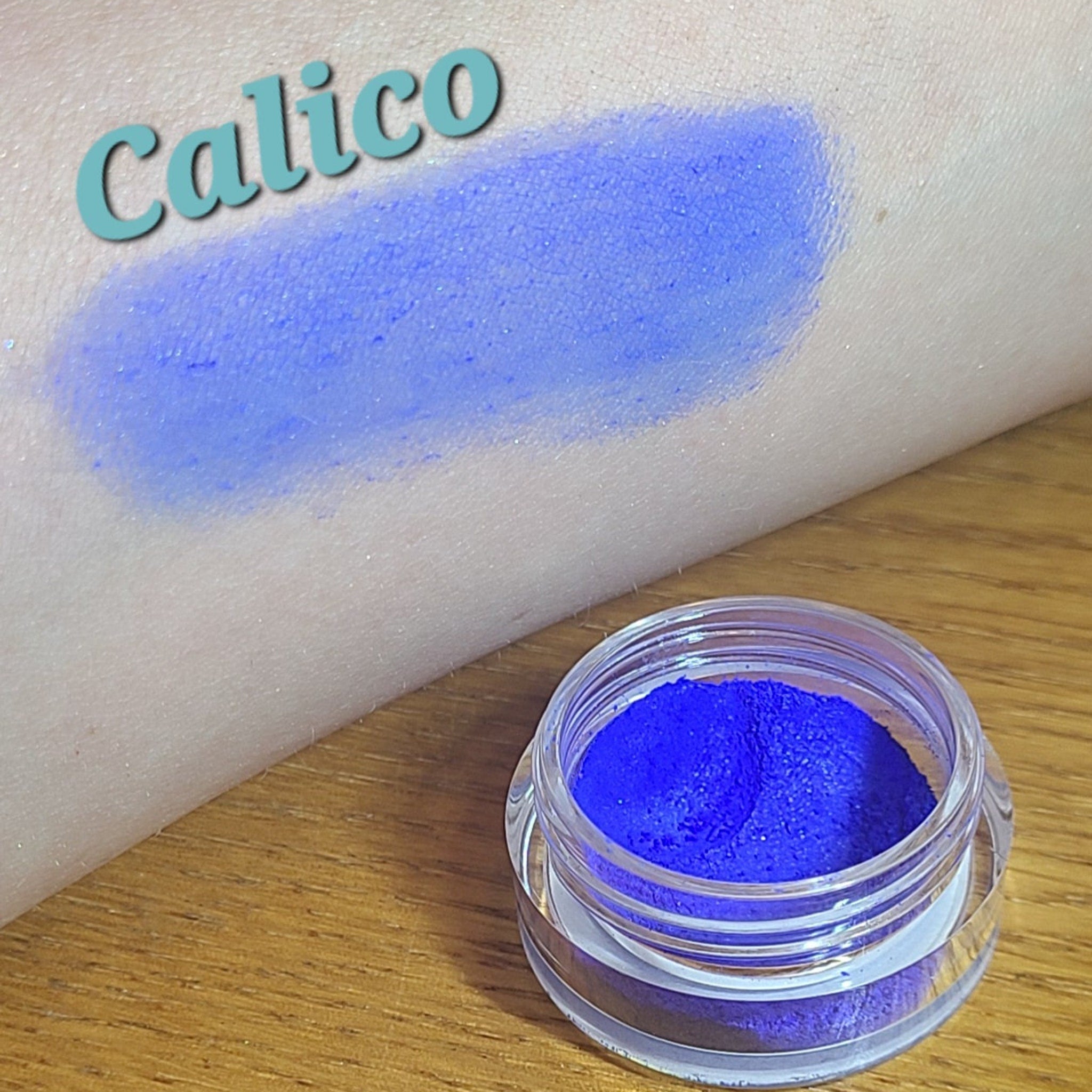 Side view of loose blue eyeshadow powder in a clear sifter jar, showcasing its fine texture and vibrant azure hue