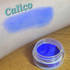 Side view of loose blue eyeshadow powder in a clear sifter jar, showcasing its fine texture and vibrant azure hue