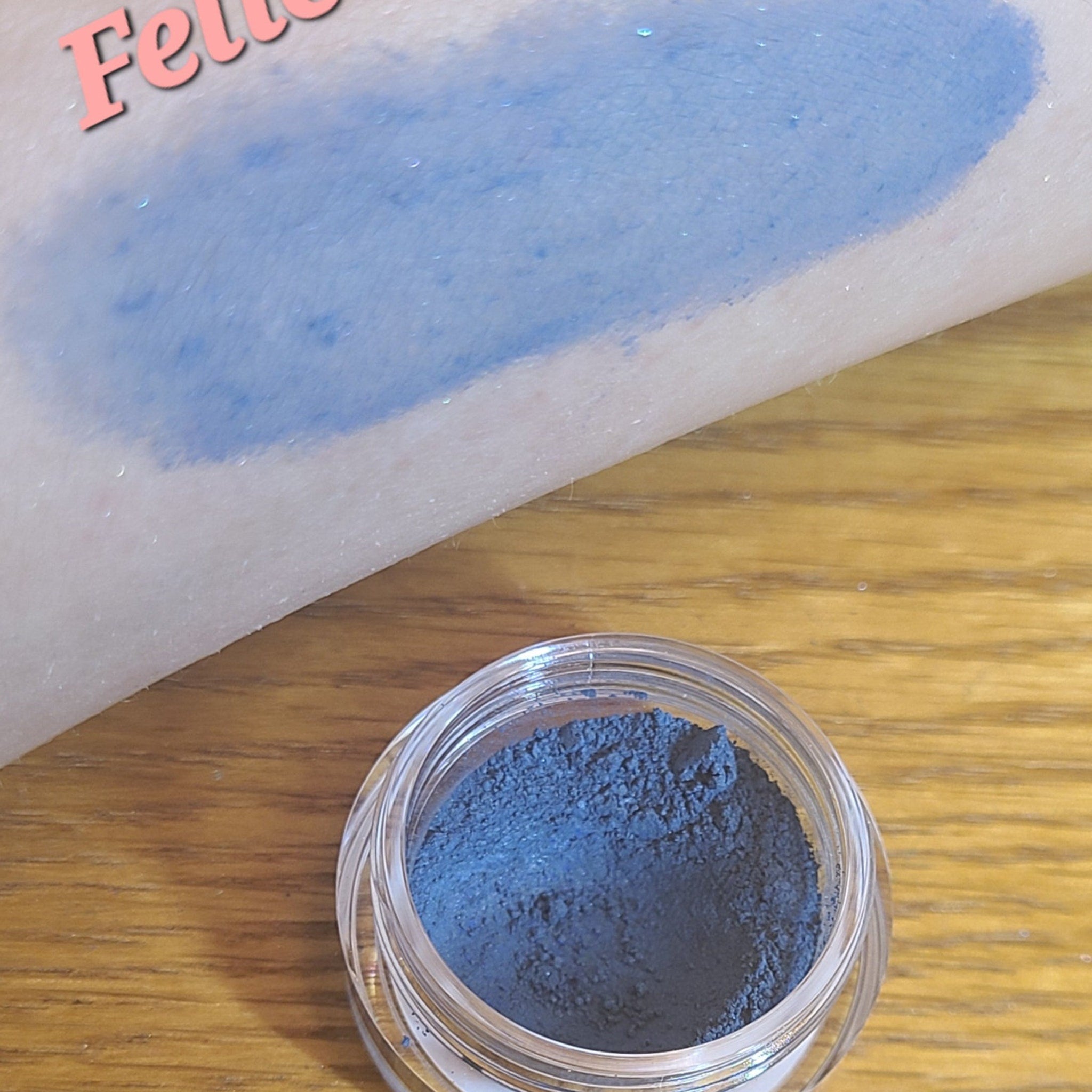 Close-up of vibrant blue loose powder eyeshadow with shimmer particles in a small glass jar