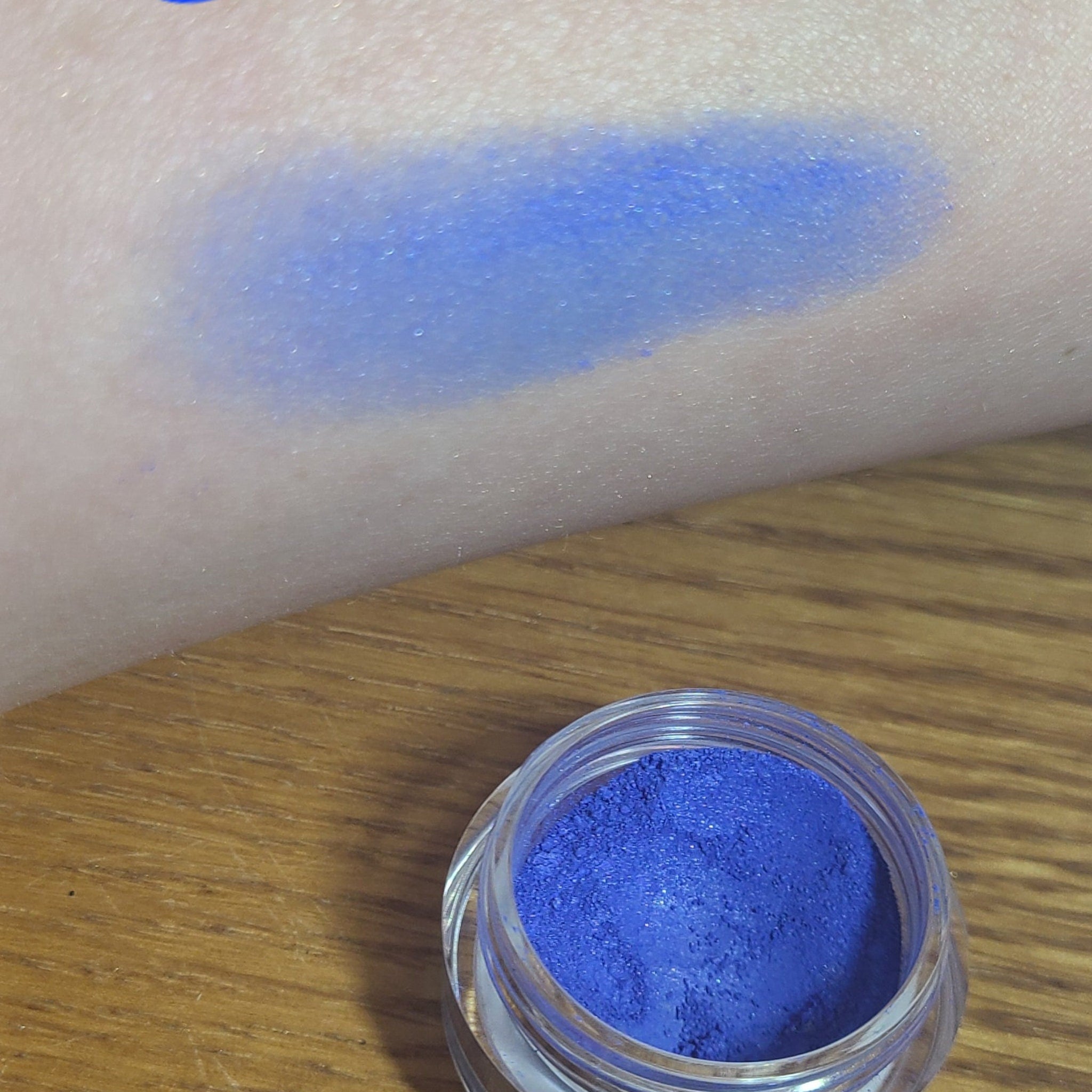 Hand applying shimmering blue loose eyeshadow with a brush for a soft, blended look