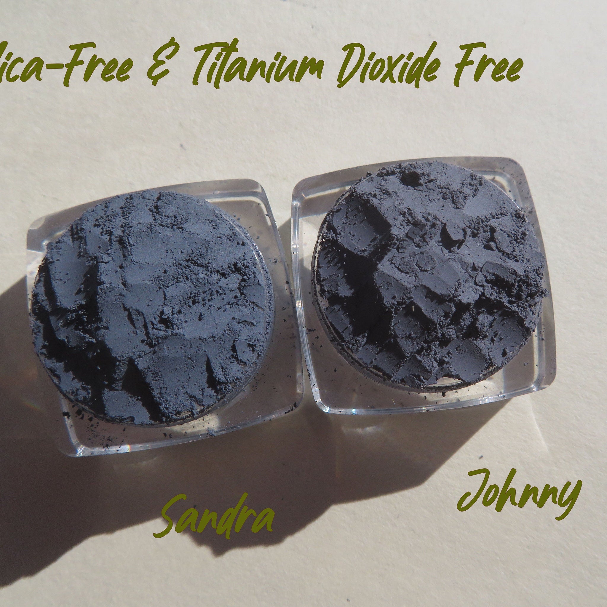 Powder eyeshadow in dark gray color, in clear plastic containers, with "Sandra" and "Johnny" text