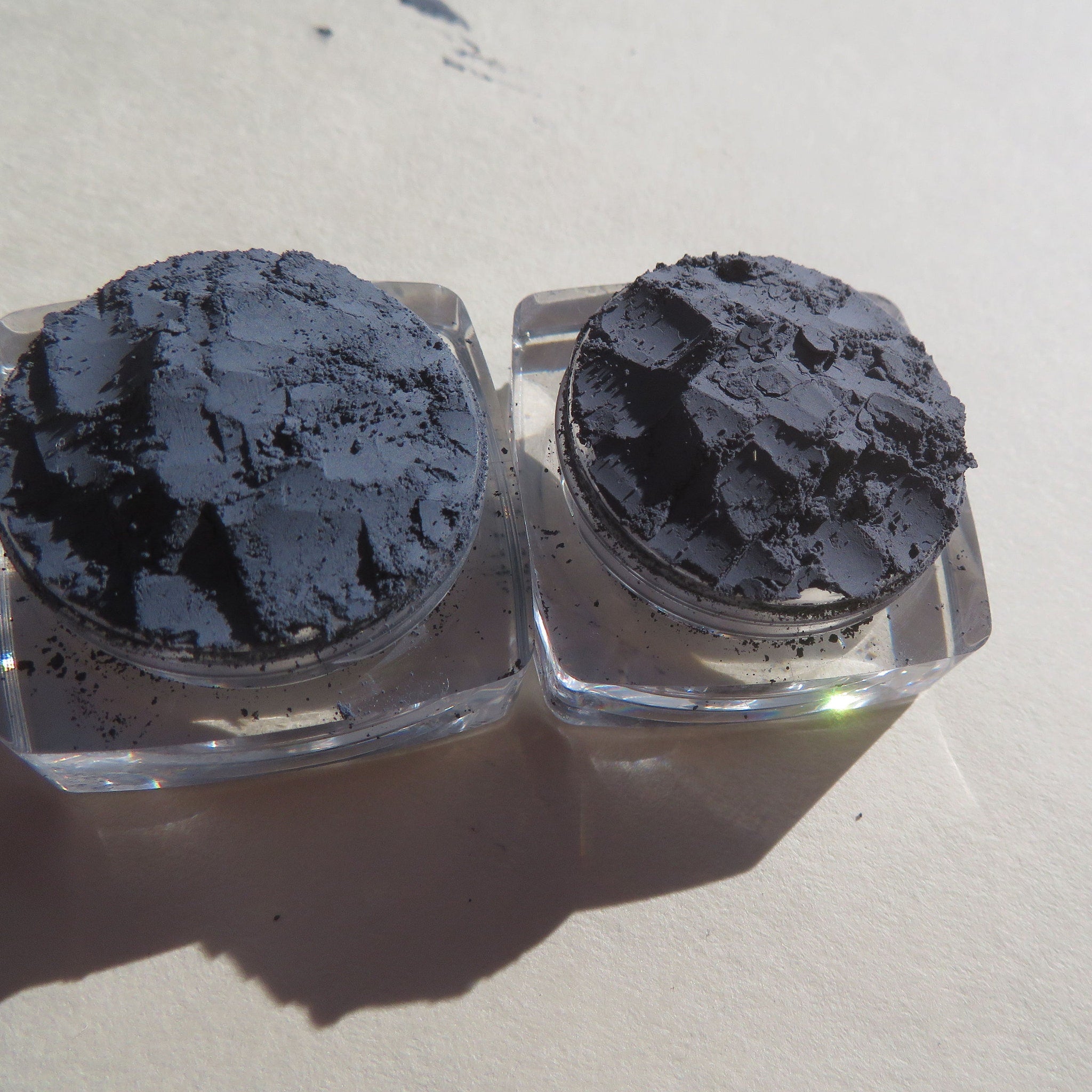 Gray powder in clear square containers, rough texture, on light surface