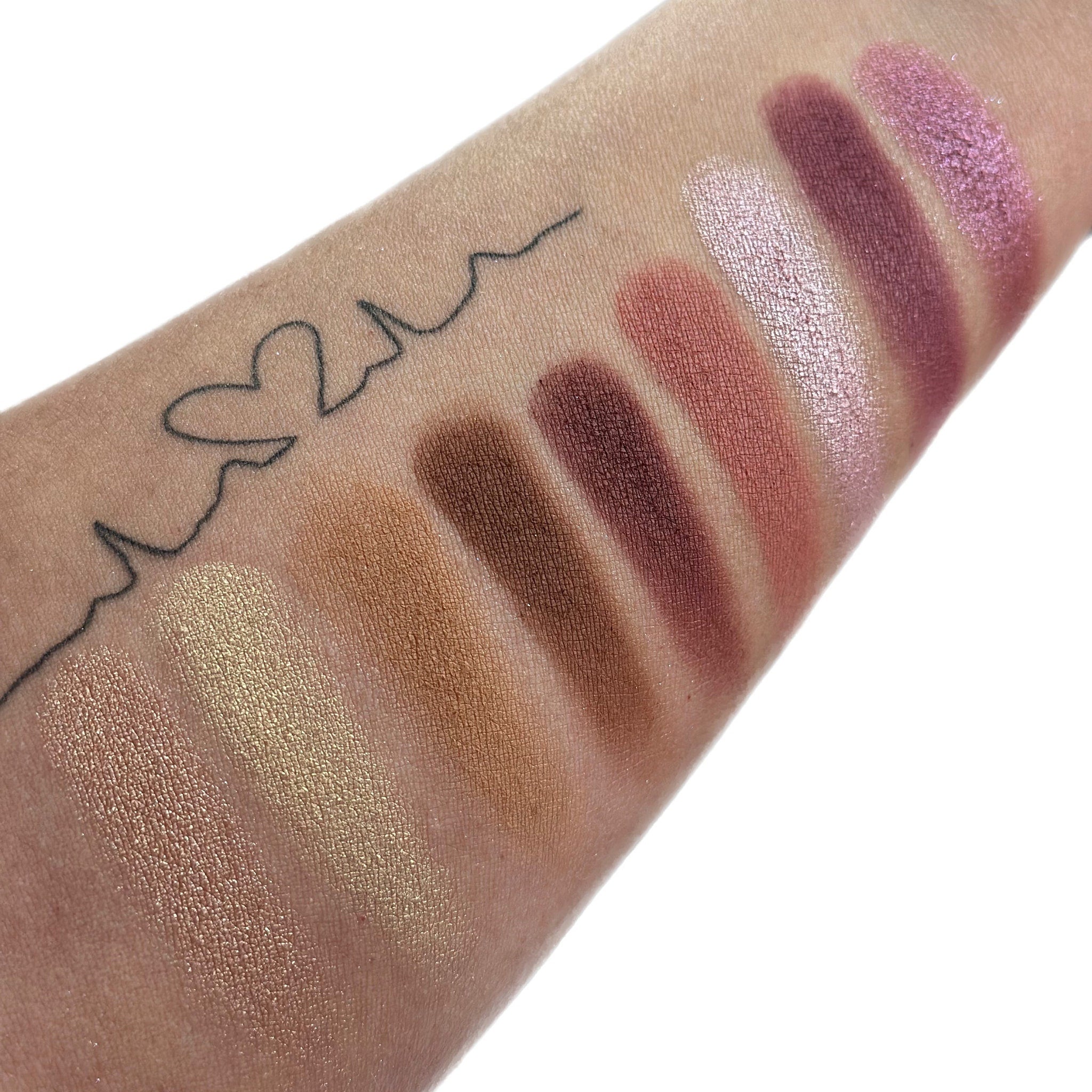 Eyeshadow swatches with various shades of brown, pink, and gold on skin, with heart tattoo detail