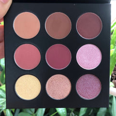 Eyeshadow palette with nine round pans in various shades of pink, brown, and gold, in a black compact