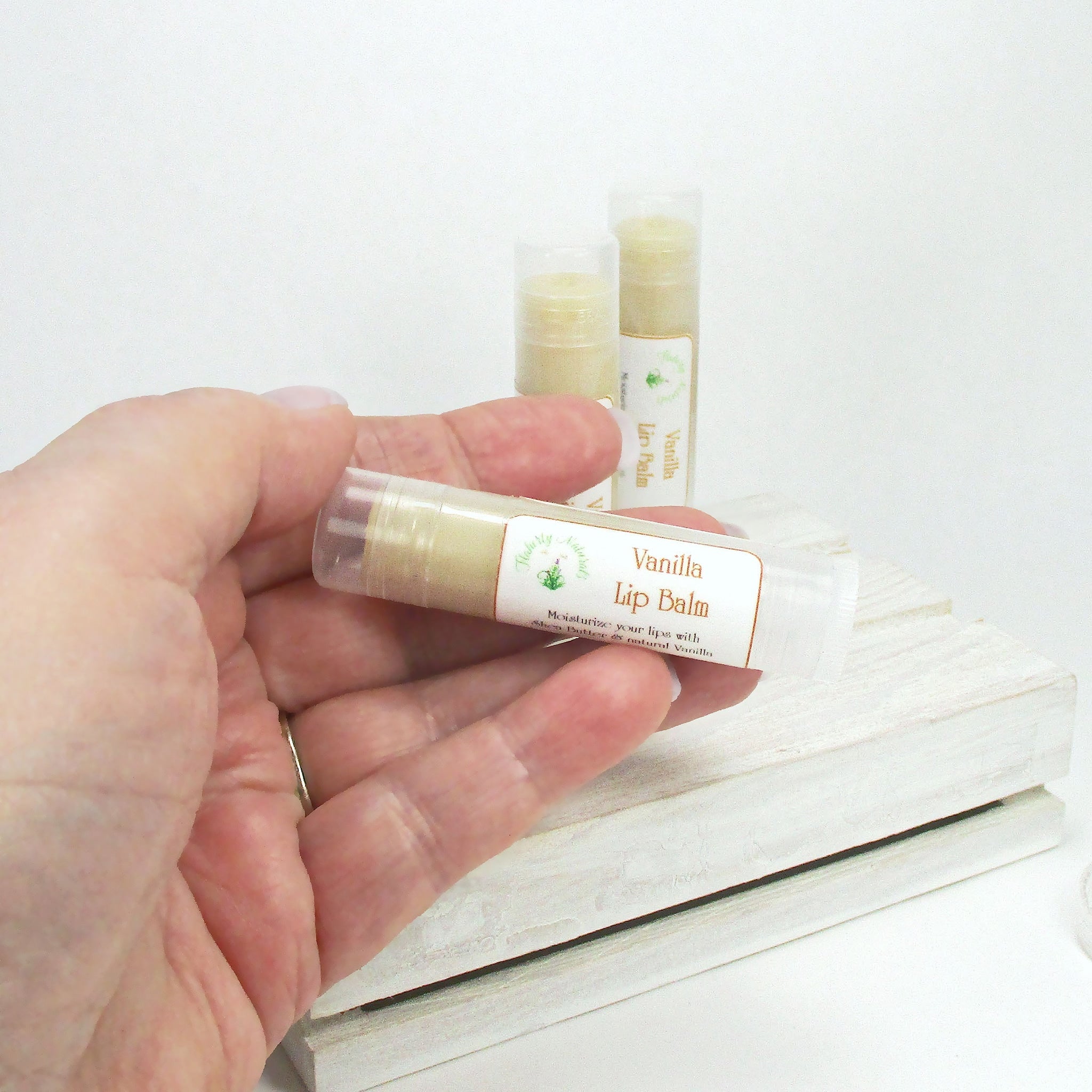 Vanilla lip balm in clear tube with white label, held in hand, on white wood