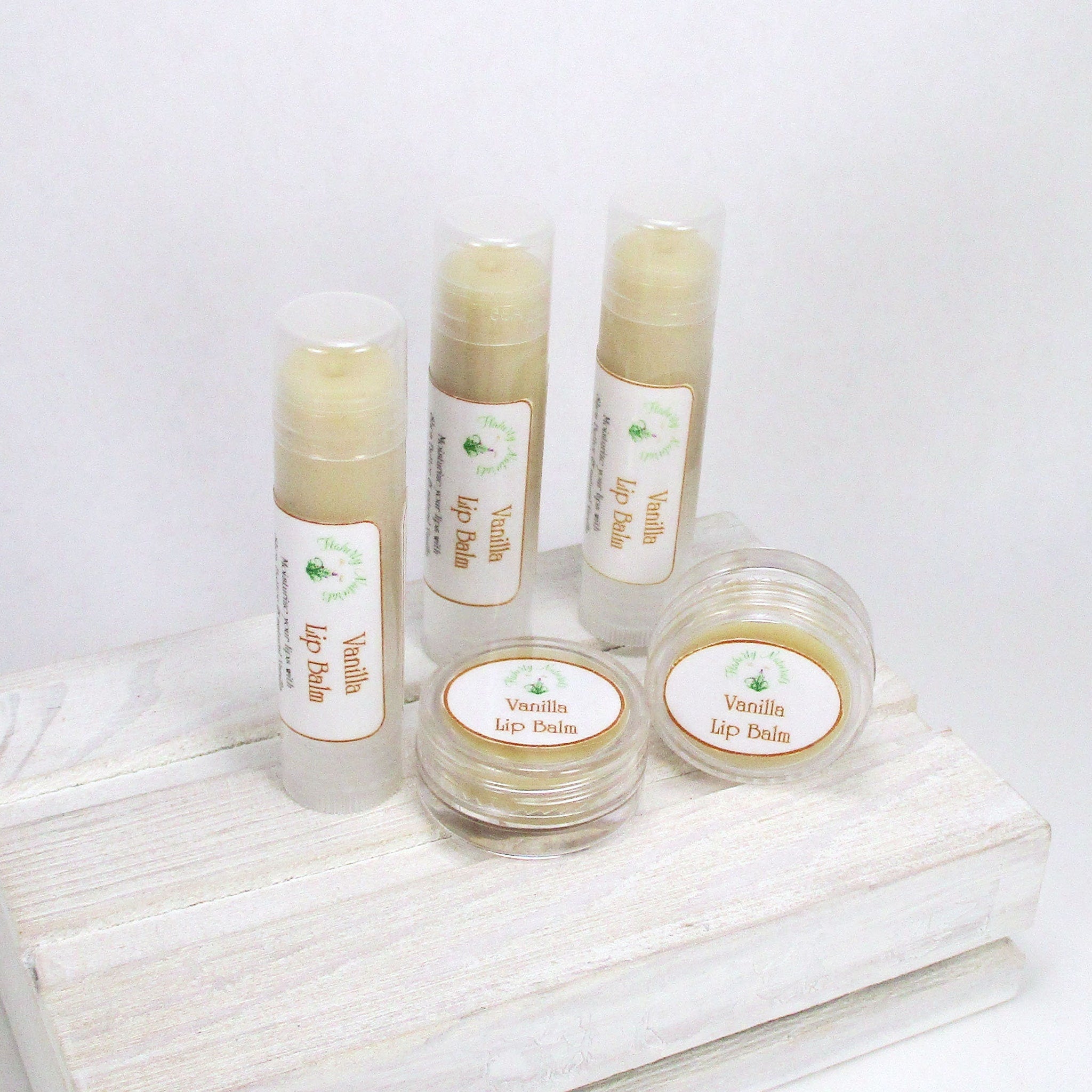 Vanilla lip balm in clear tubes and jars, with white labels, on a white wooden surface