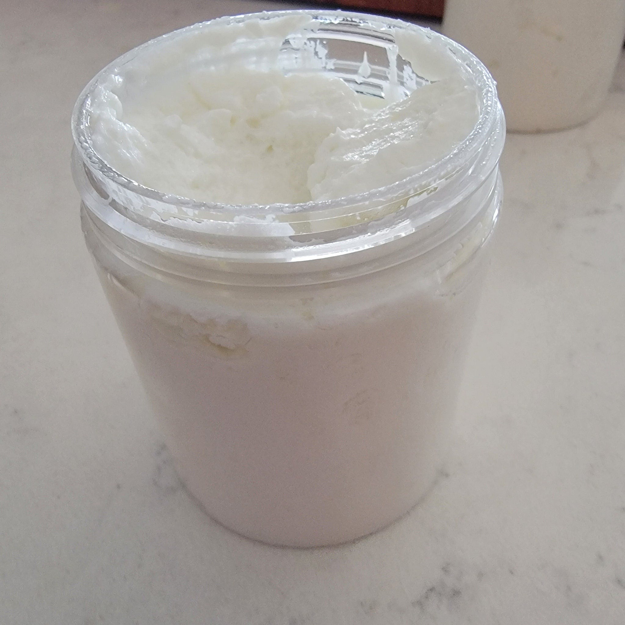 Creamy white substance in clear plastic jar, partially open, on a white surface