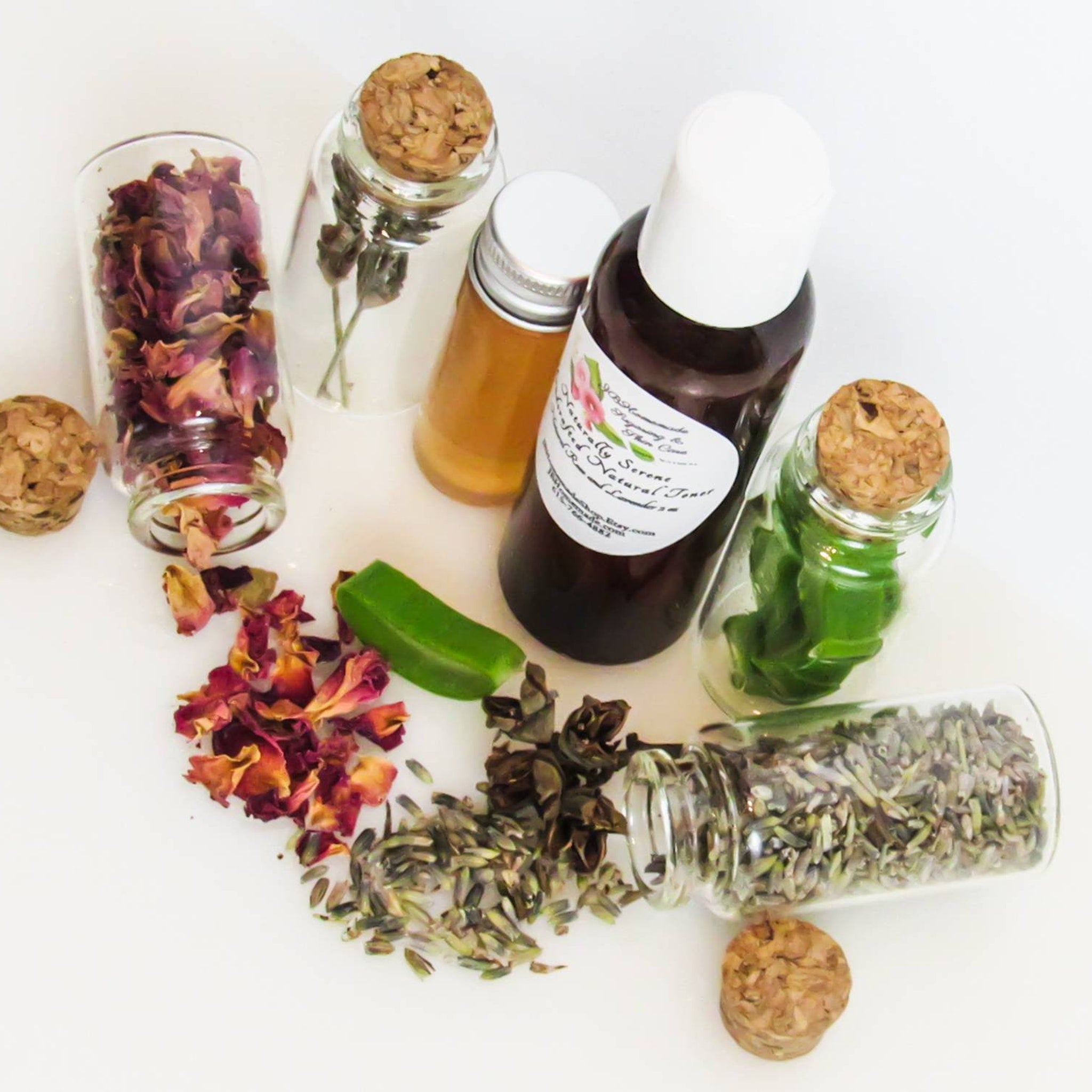 Dried rose petals, lavender, and herbs in glass bottles with cork tops, on white surface