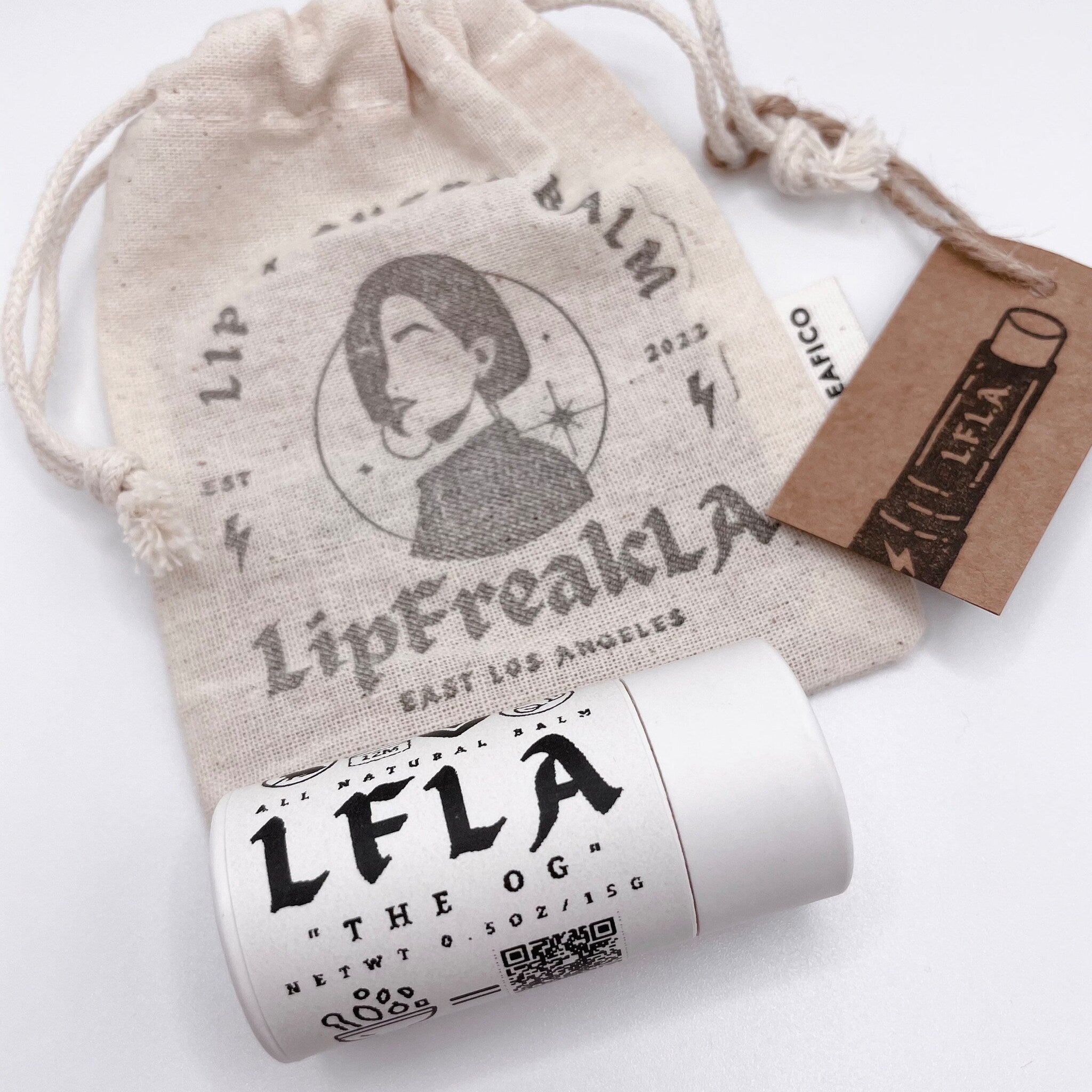 Lip balm tube with white and black text, beige canvas bag with printed design and brown tag with LFLA logo