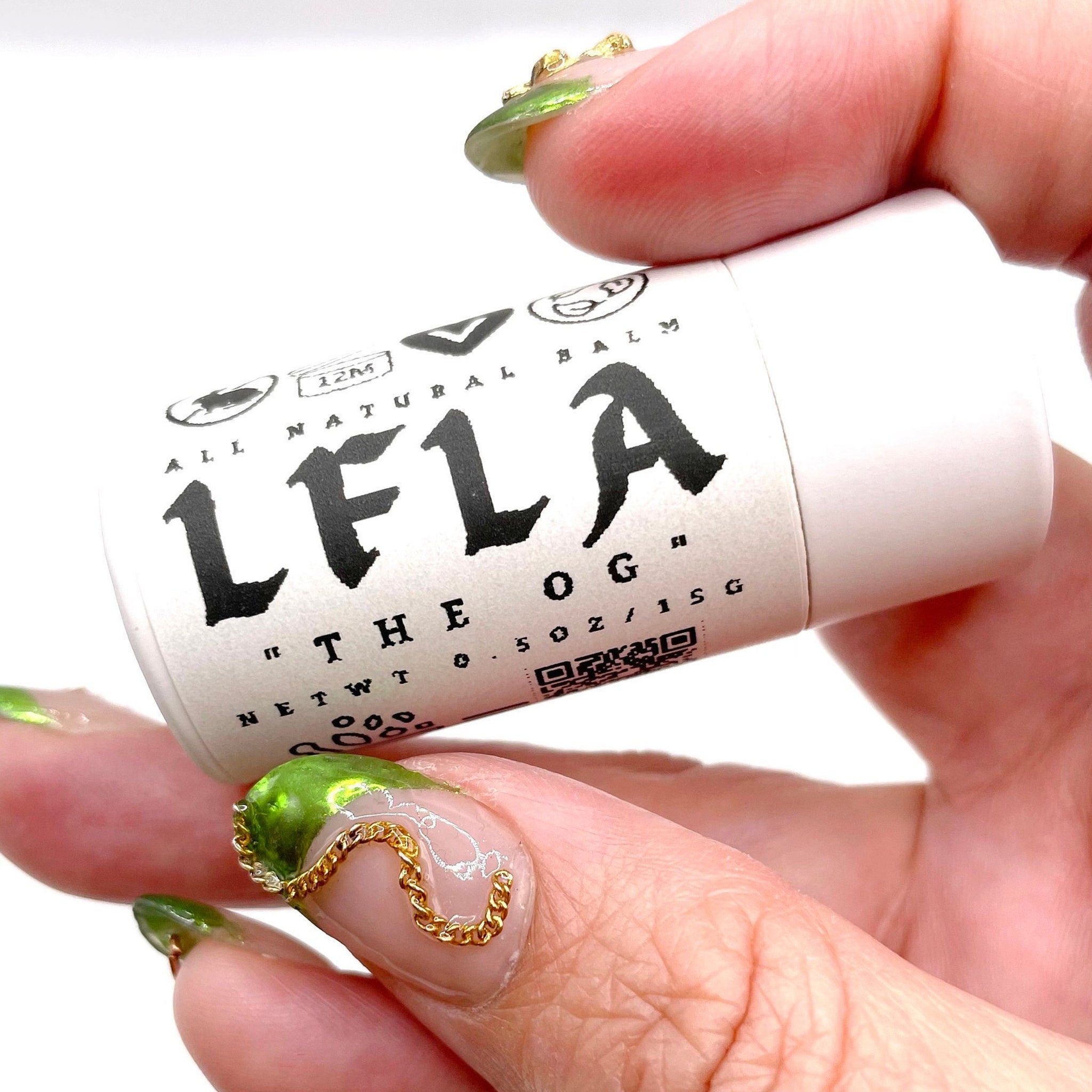 Lip balm tube with white label and black text, held in hand with green nails, LFLA brand visible
