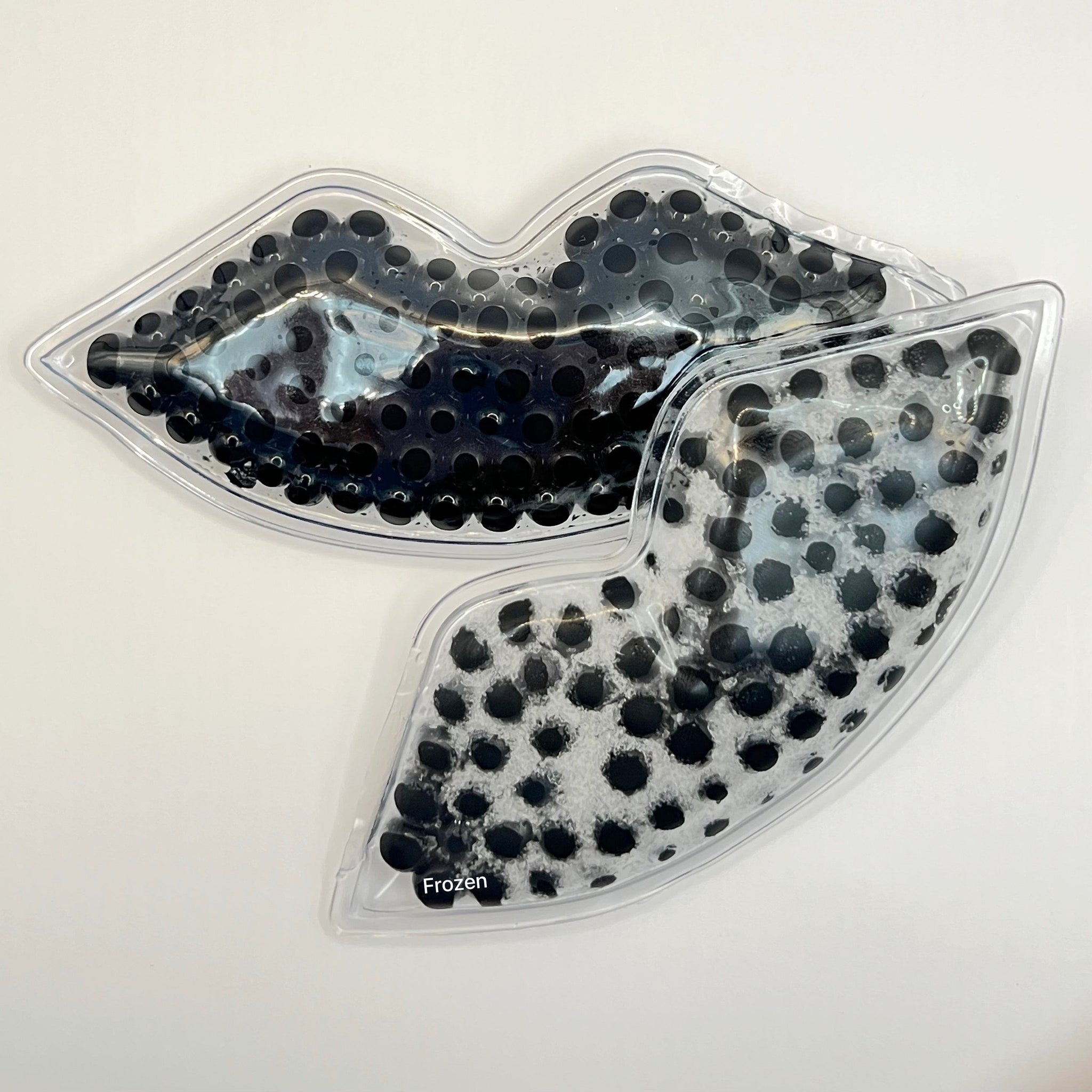Lip-shaped gel pack, clear plastic, black bead filling, "Frozen" text visible.