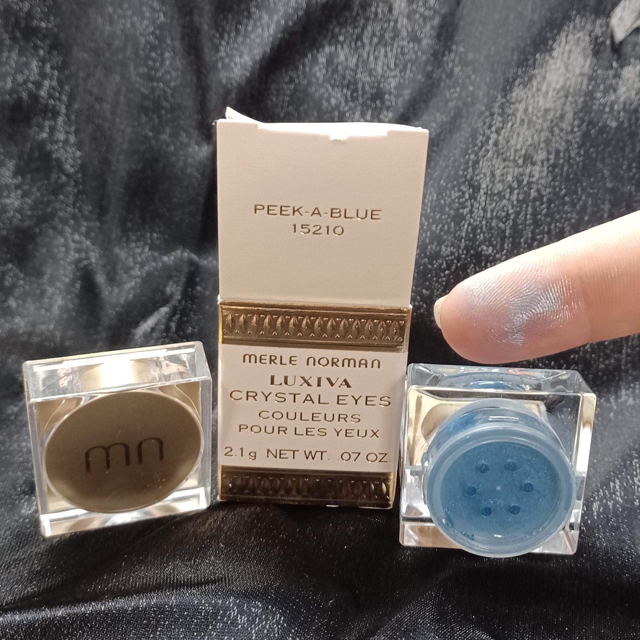 Merle Norman loose glitter eyeshadow pot with gold lid, showcasing sparkling powder through clear packaging