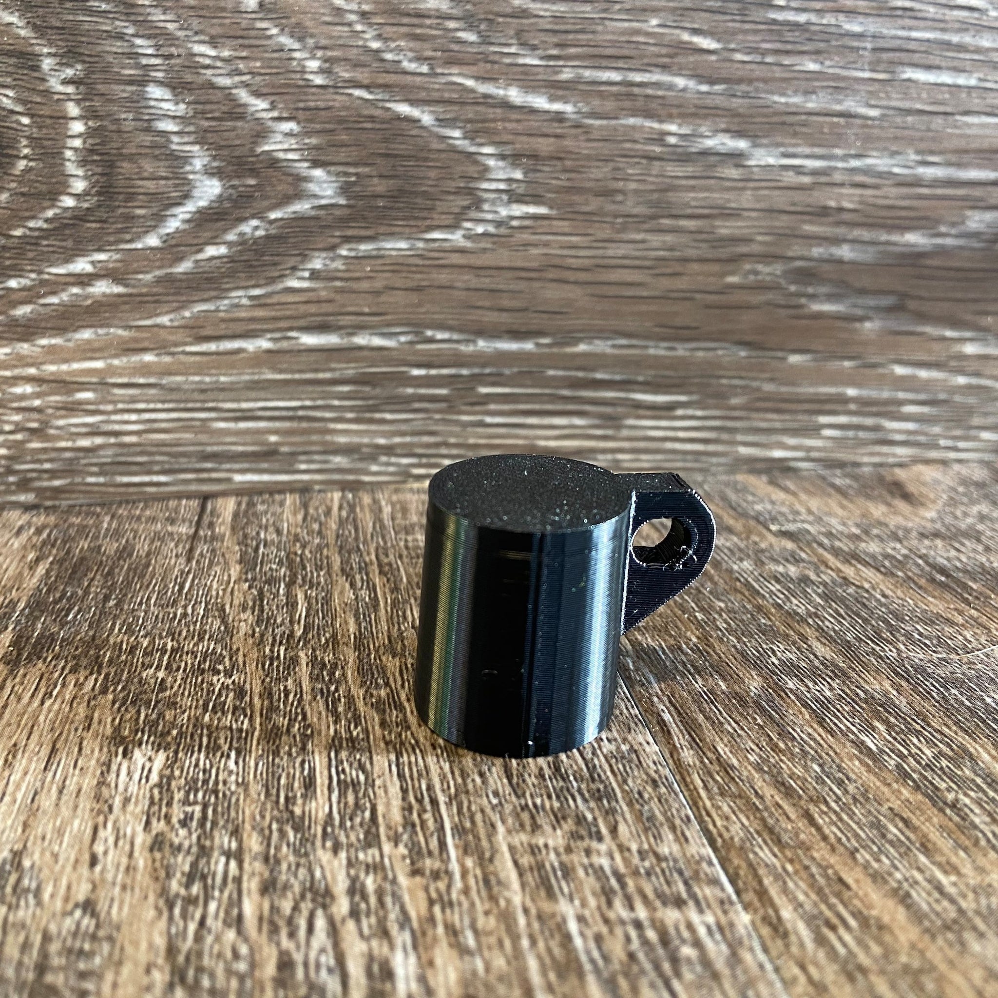 Black cylindrical object with handle, 3D printed, on wood surface
