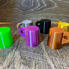 Miniature mugs in various colors, 3D printed with textured surfaces, arranged on wood surface