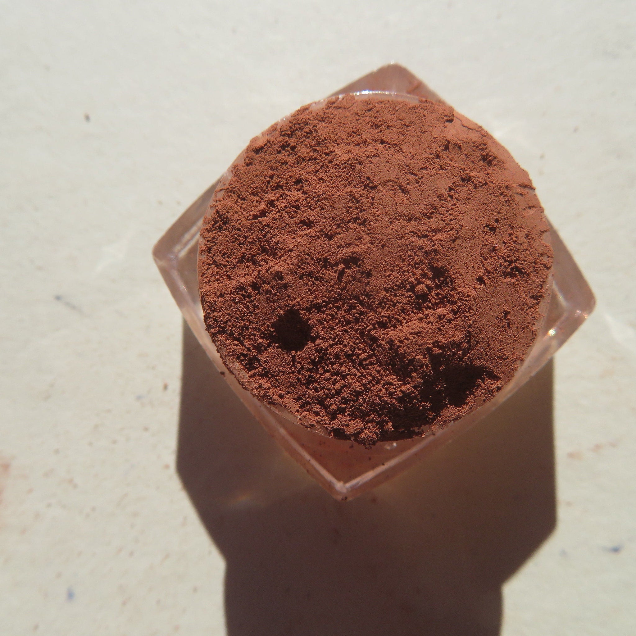 Close-up of matte orange-brown loose mineral eye shadow with fine mica particles in a jar
