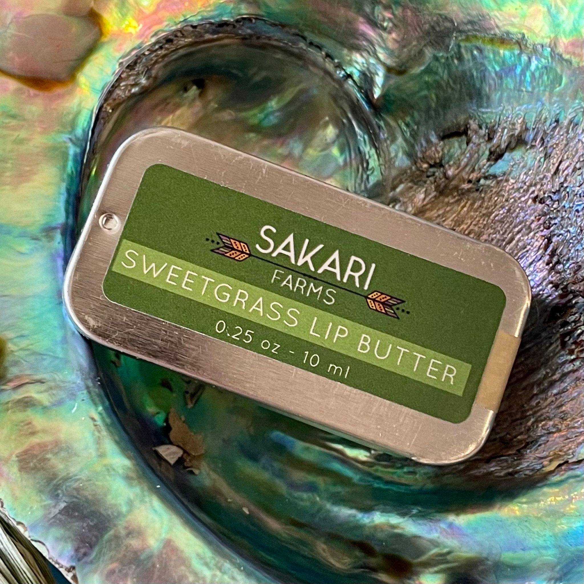 Lip butter tin with green label, silver metal edges, and Sakari Farms brand name visible