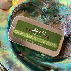 Lip butter tin with green label, silver metal edges, and Sakari Farms brand name visible