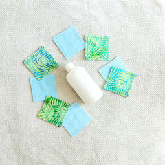 Makeup remover pads, blue and tropical print fabric, arranged with lotion bottle on white towel
