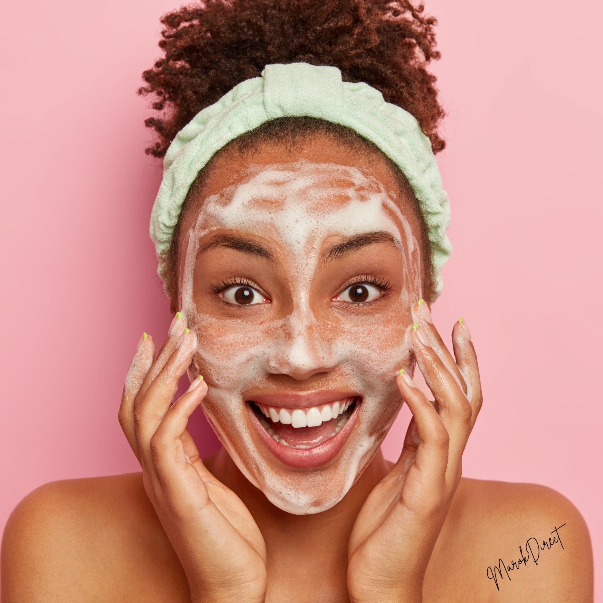 Facial cleanser with white foam, mint headband, and smiling woman applying to face