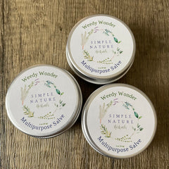 Multipurpose salve tins with white labels, silver metal, and Simple Nature Herbals text on wood background