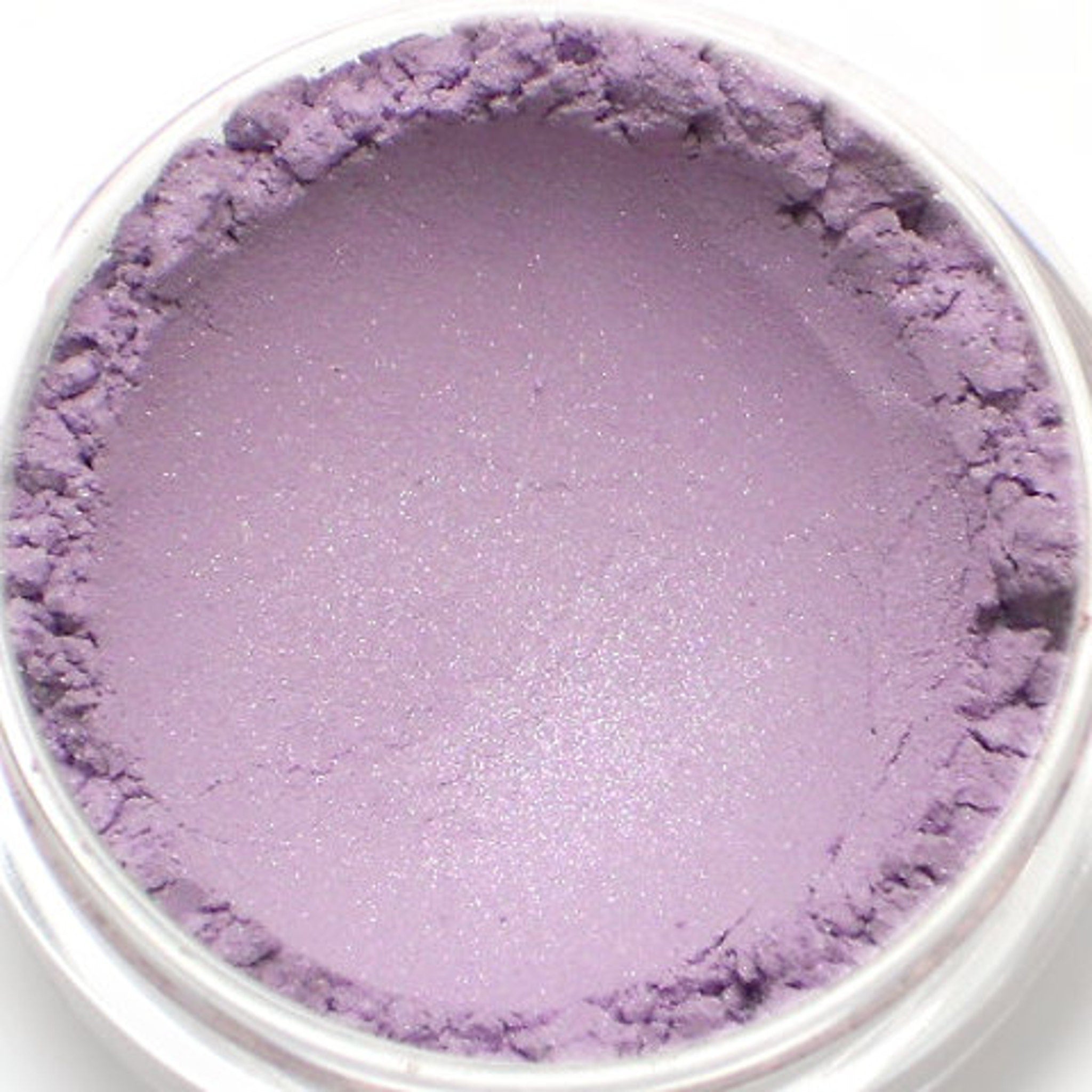 Purple powder eyeshadow in a clear container, with a shimmery finish and textured edges