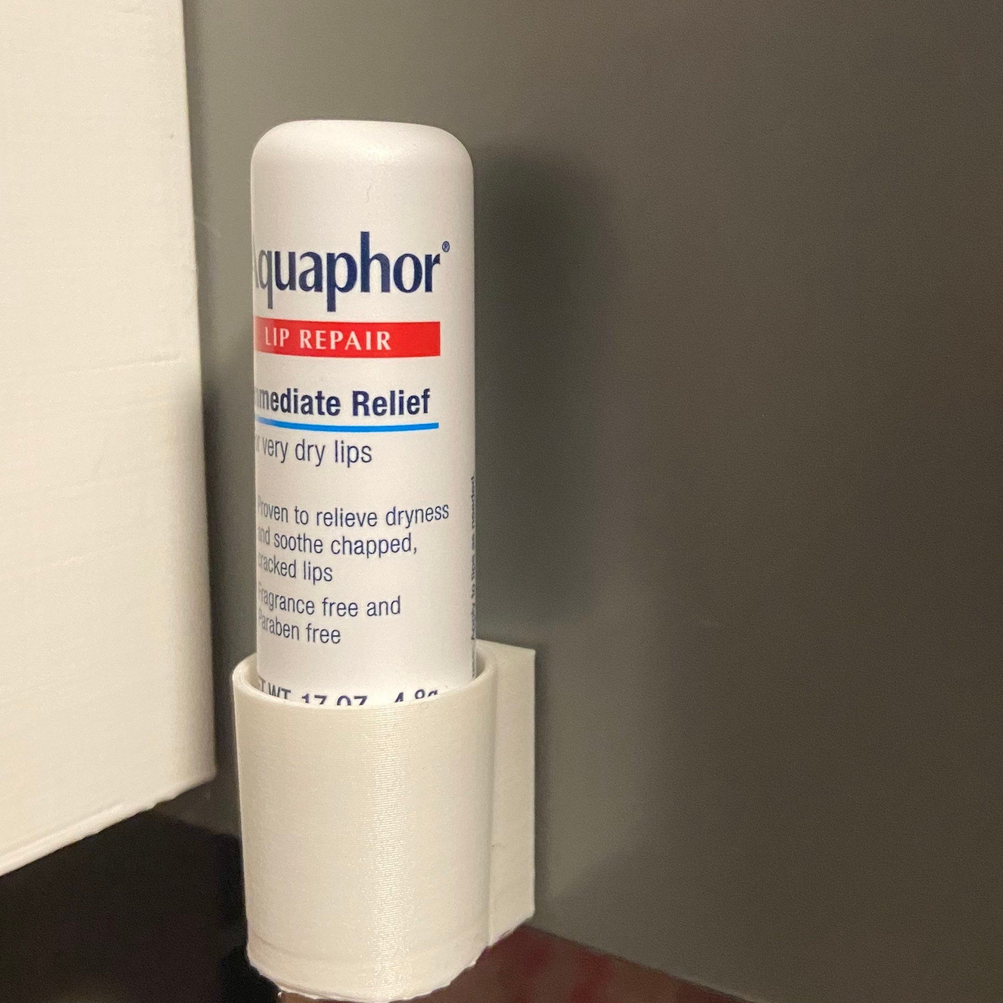 Lip repair product in white tube with red and blue text, held in a white holder, Aquaphor brand visible