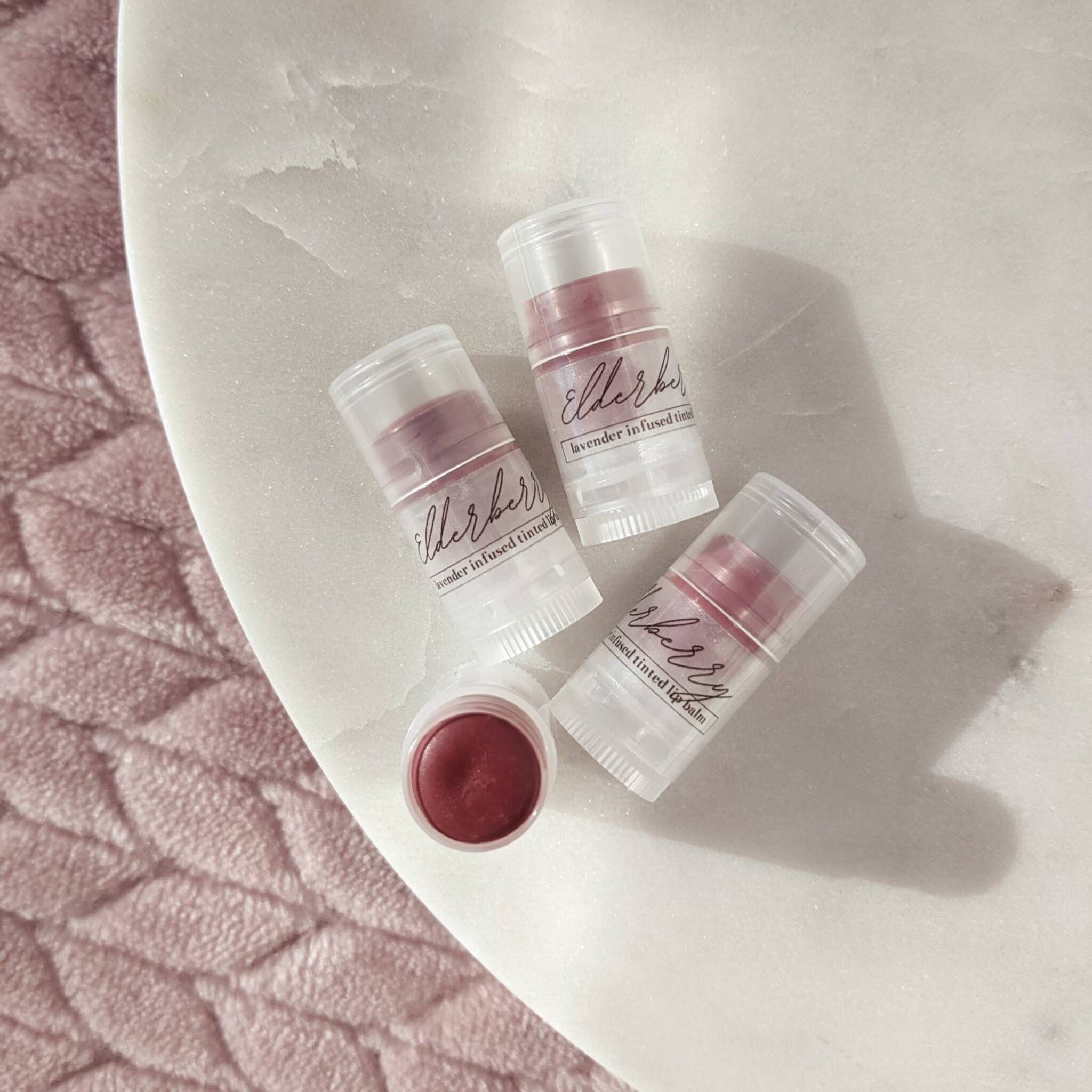 Lip balm tubes with clear plastic, purple tint, and "elderberry" label text on white marble surface