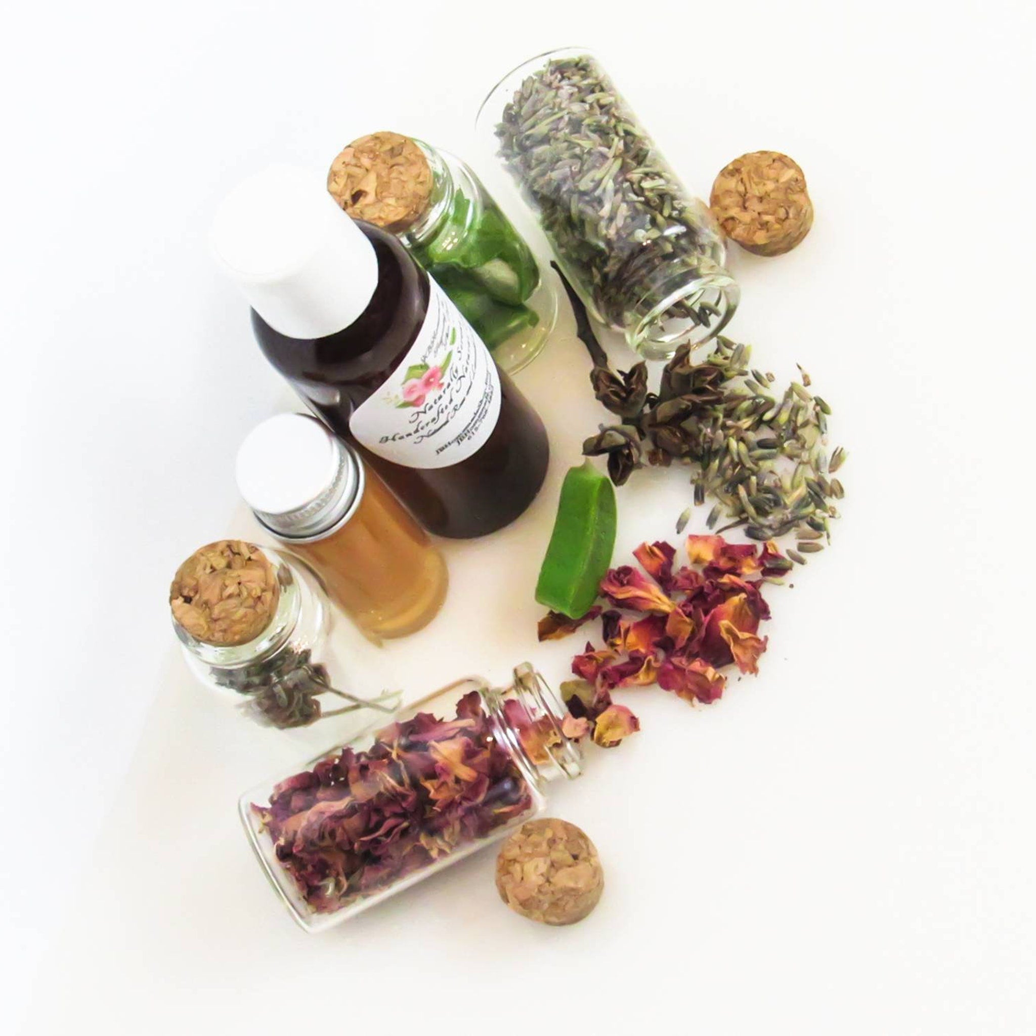 Bottles with corks and herbs, glass jars with dried rose petals, and a green soap bar on white background