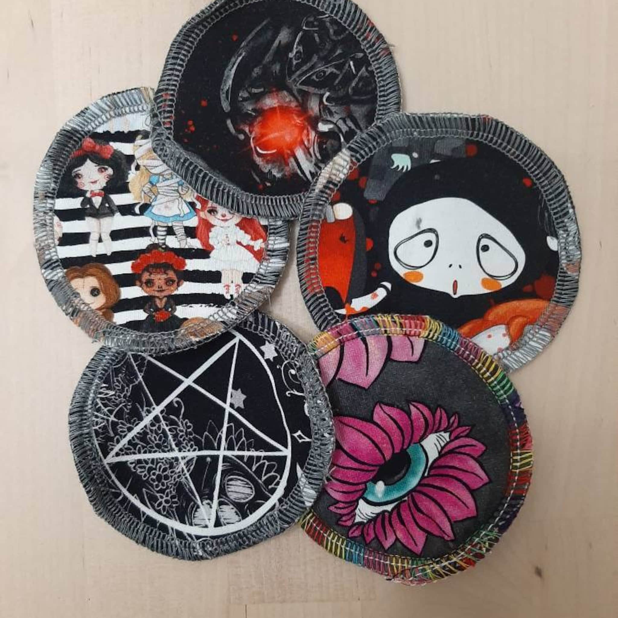 Reusable pads with black, white, and colorful patterns, featuring dolls, spider, and eye designs